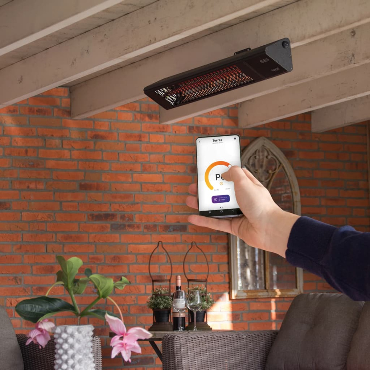 Une main tenant un téléphone contrôlant un radiateur infrarouge extérieur. Lueur rouge en arrière-plan.
