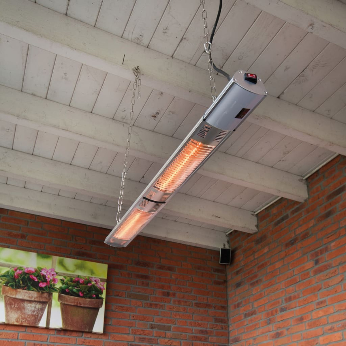Infrared heater hanging from a white wooden ceiling, near a brick wall and flowers.