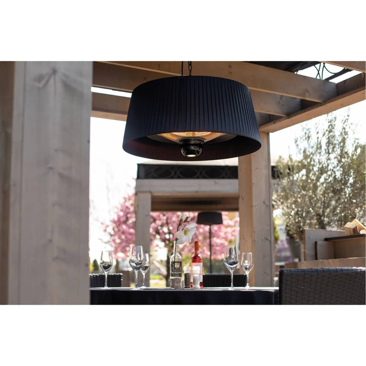 Buiten eettafereel met een zwarte hanglamp, tafelsetting en vage achtergrond van bomen.
