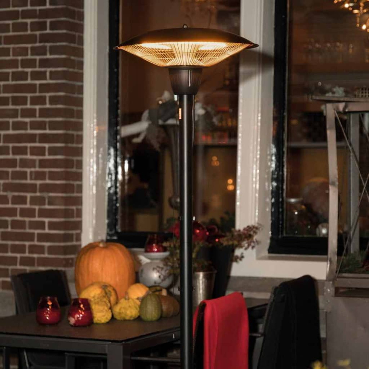 Een terrasverwarmer die bij een tafel met pompoenen, kalebassen en kaarsen staat. Een raam op de achtergrond.