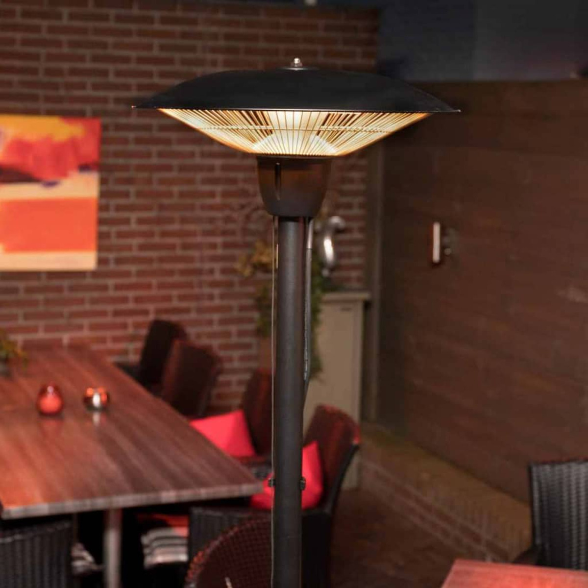 Een zwarte buitenkachel met een groot bovenstuk staat op een terras. Een tafel en stoelen staan op de achtergrond.