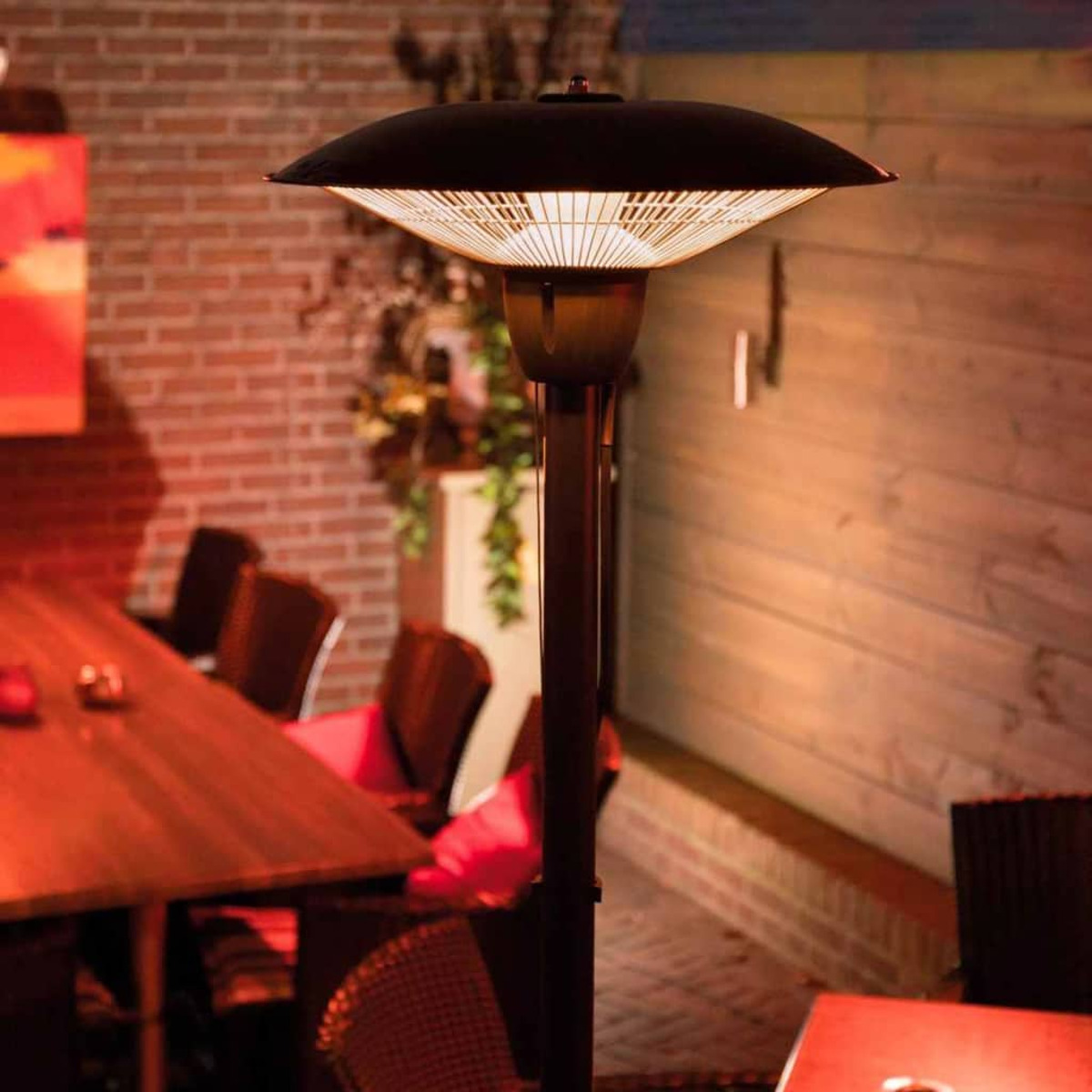 Buitenverwarming met een zwarte bovenkant en een bakstenen muur op de achtergrond. Er is een tafel en stoelen in de scène.