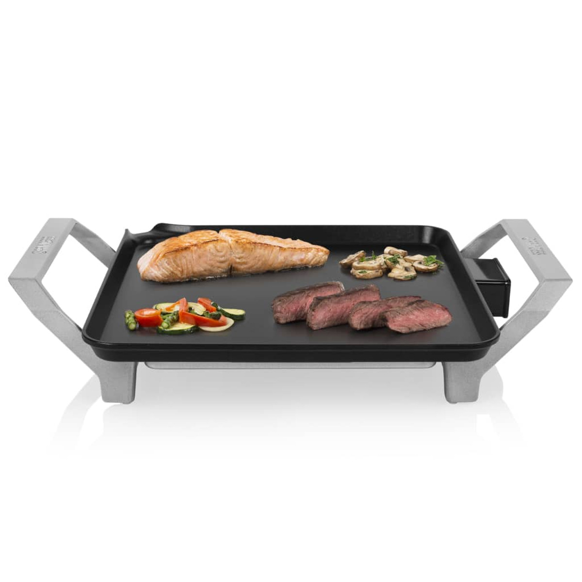 Una parrilla eléctrica con salmón cocido, bistec, verduras y champiñones en una superficie negra.