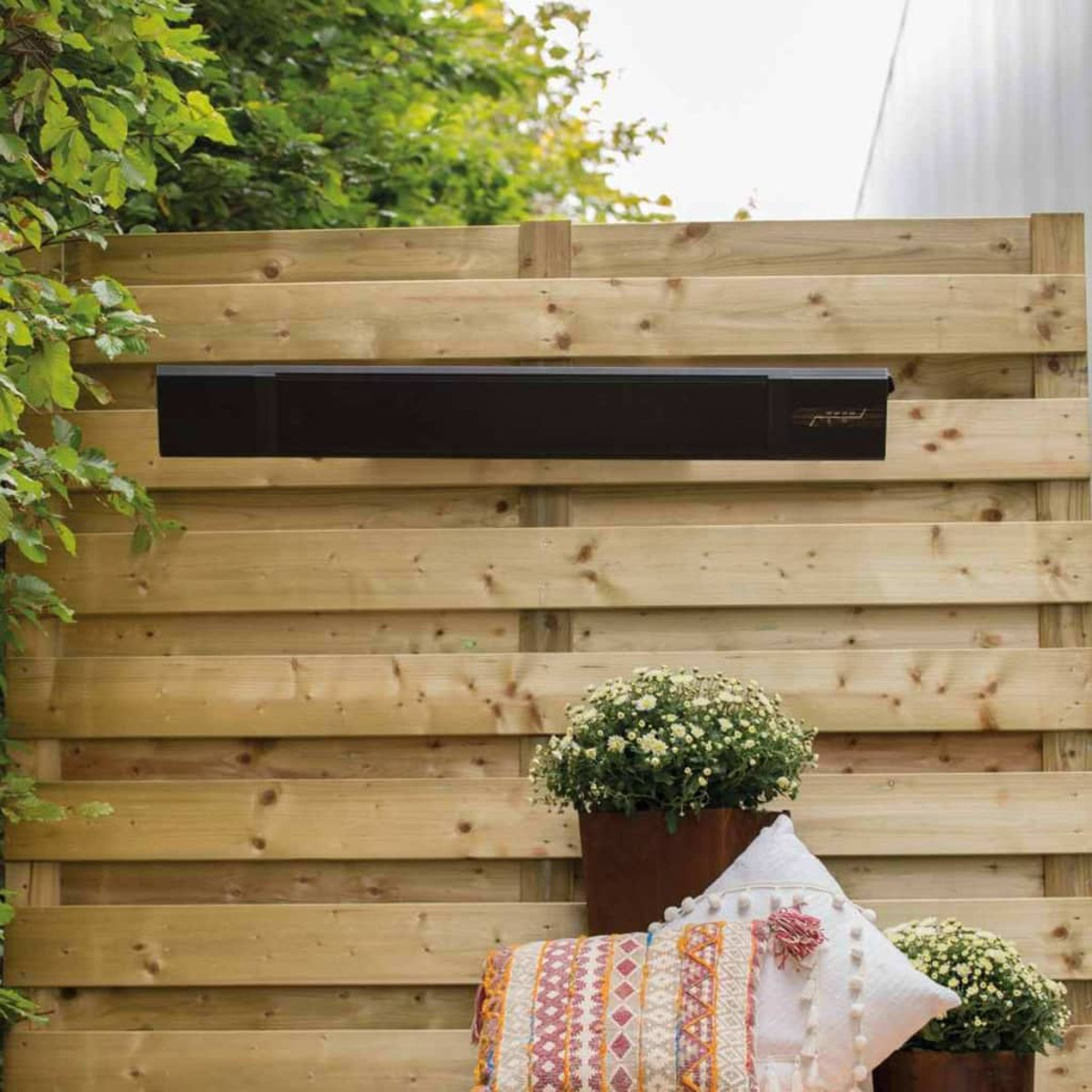 A black heater is mounted on a wooden fence. The brand name is visible. 