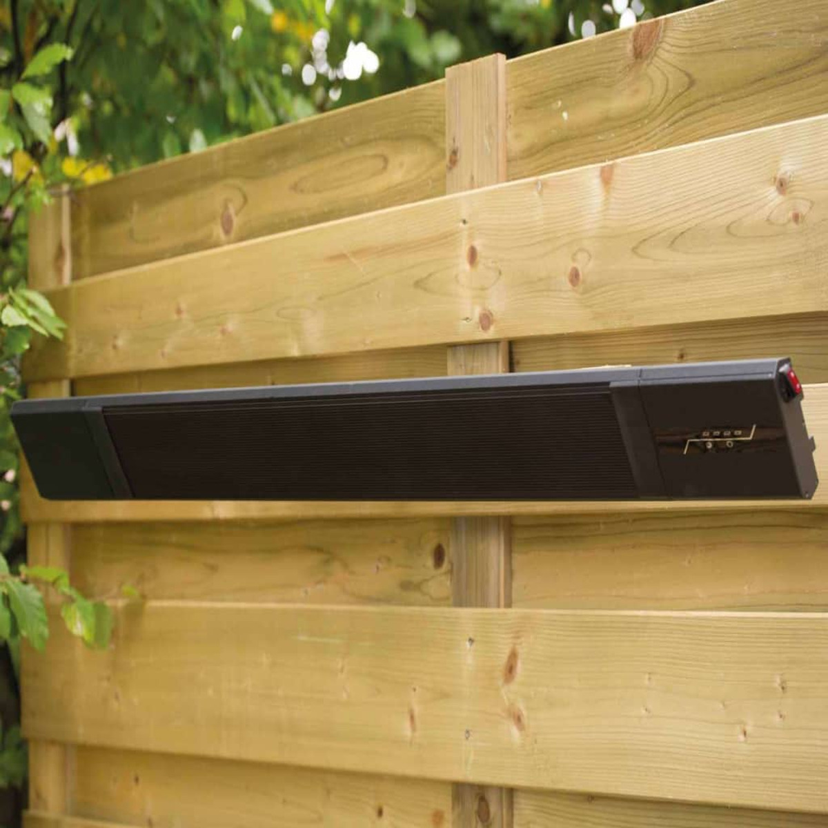 Black outdoor heater mounted on a wooden fence. Green background.