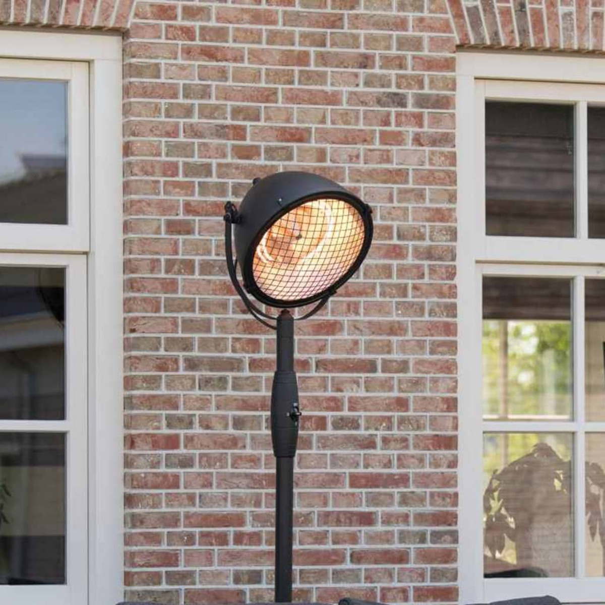 Zwarte buitenkachel op een standaard, met een rode bakstenen muur als achtergrond.