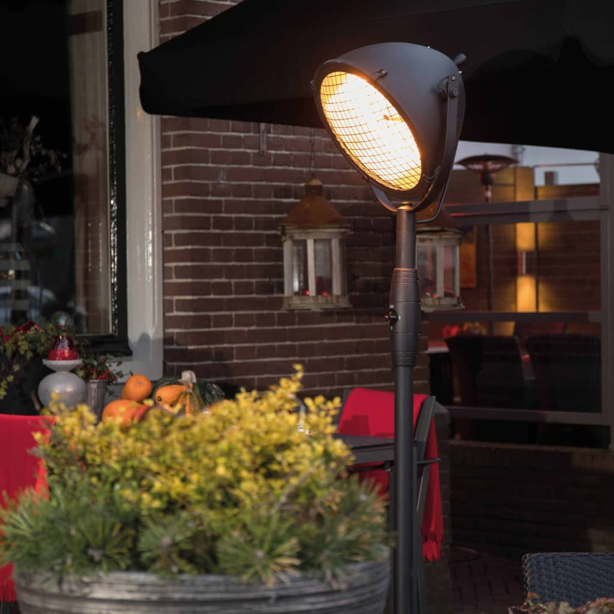 Buitenverwarmer met fel licht. Een bloempot op de voorgrond. Bakstenen muur op de achtergrond.