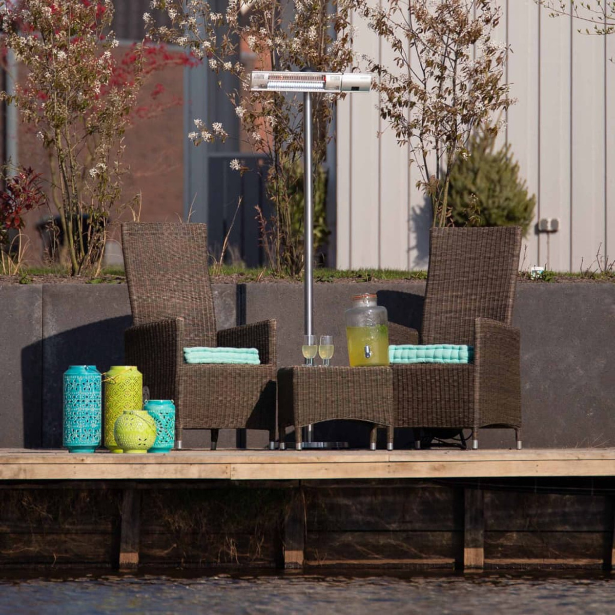 Buitenscène met stoelen, een tafel, lantaarns en een kachel, dichtbij water.