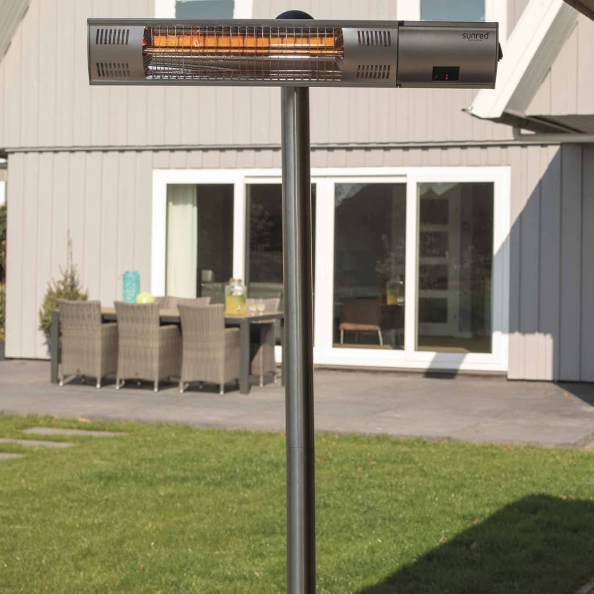 Een terrasverwarmer op een standaard in een tuin. Een huis en een tafel staan op de achtergrond.