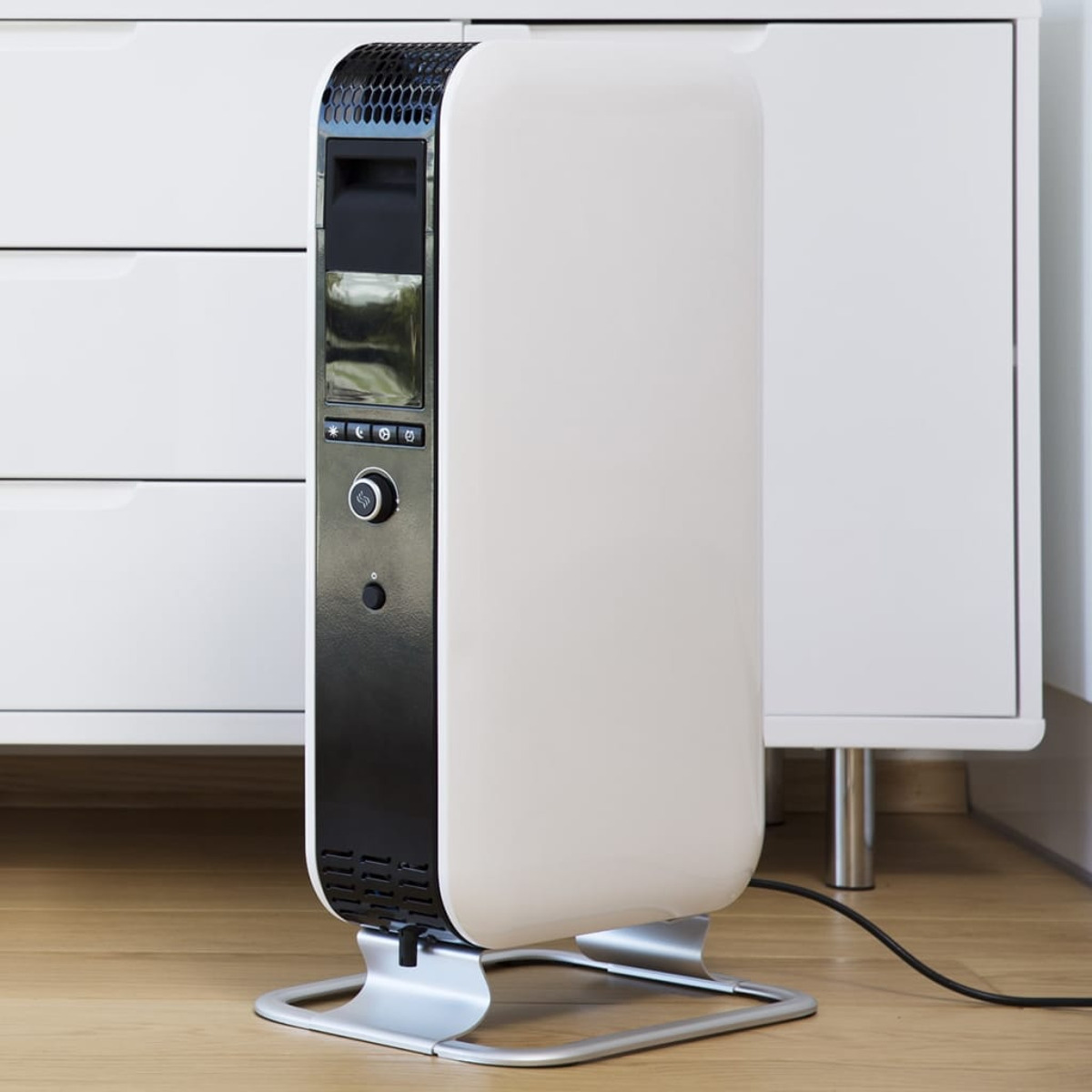 Biało-czarny grzejnik elektryczny na drewnianej podłodze, obok białej szafki w pokoju.