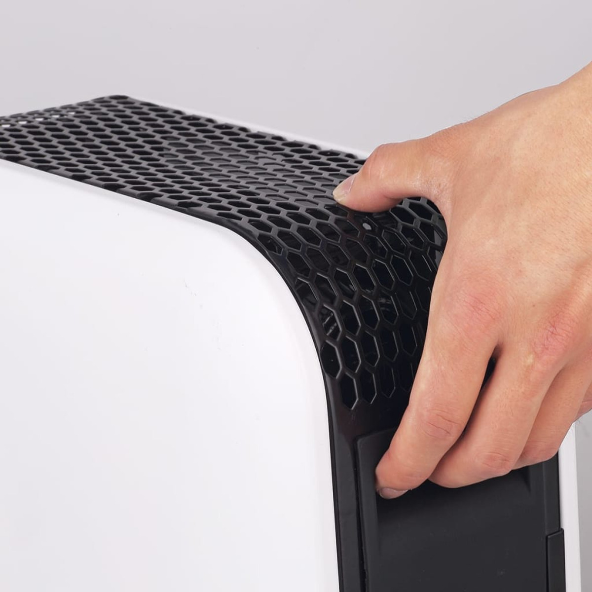 Ręka otwierająca czarny panel na białym urządzeniu.