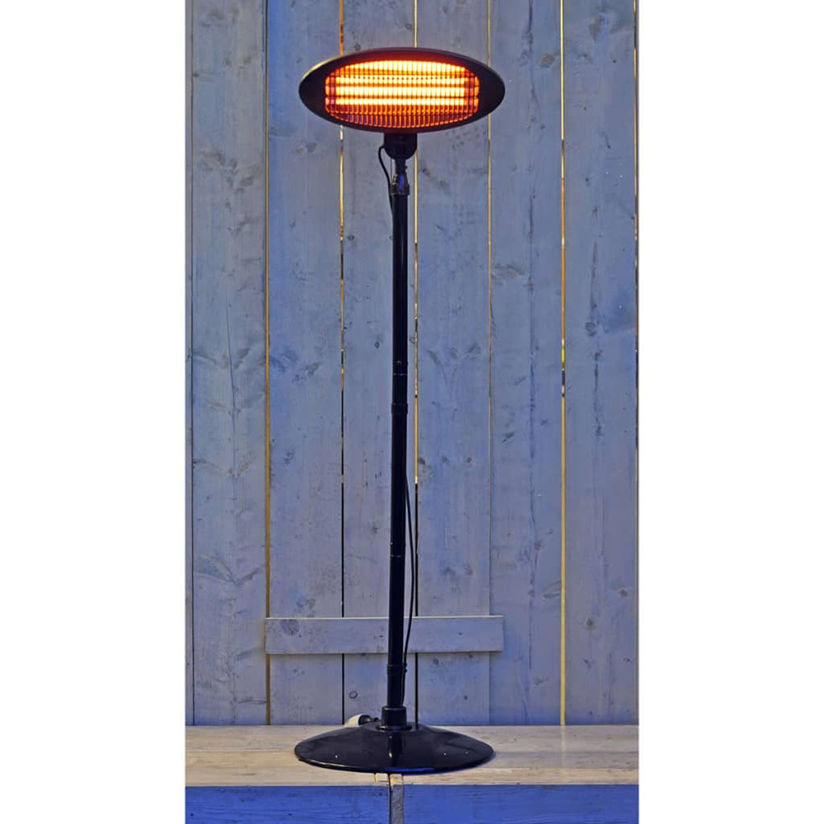 Schwarzer Außenheizer auf einem Ständer. Der Heizer ist oval und leuchtet orange. Der Hintergrund ist aus Holz.