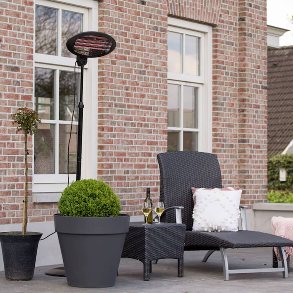 Szene im Freien mit einem Terrassenheizstrahler, einem Tisch und einem Stuhl in der Nähe einer Ziegelmauer und Fenster.