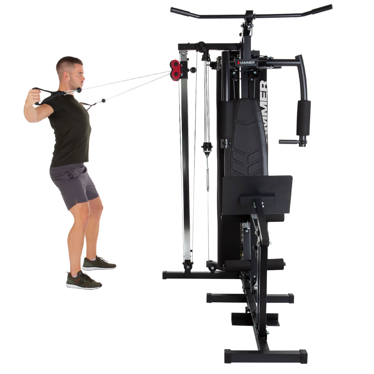 Mann benutzt ein schwarzes und silbernes Home-Gym. Er zieht an Kabeln. Der Hintergrund ist eine weiße Wand.