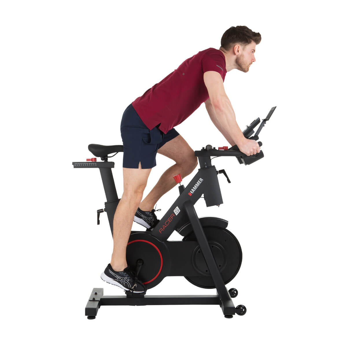 Mann auf einem stationären Heimtrainer. Er trägt ein rotes Hemd und blaue Shorts.