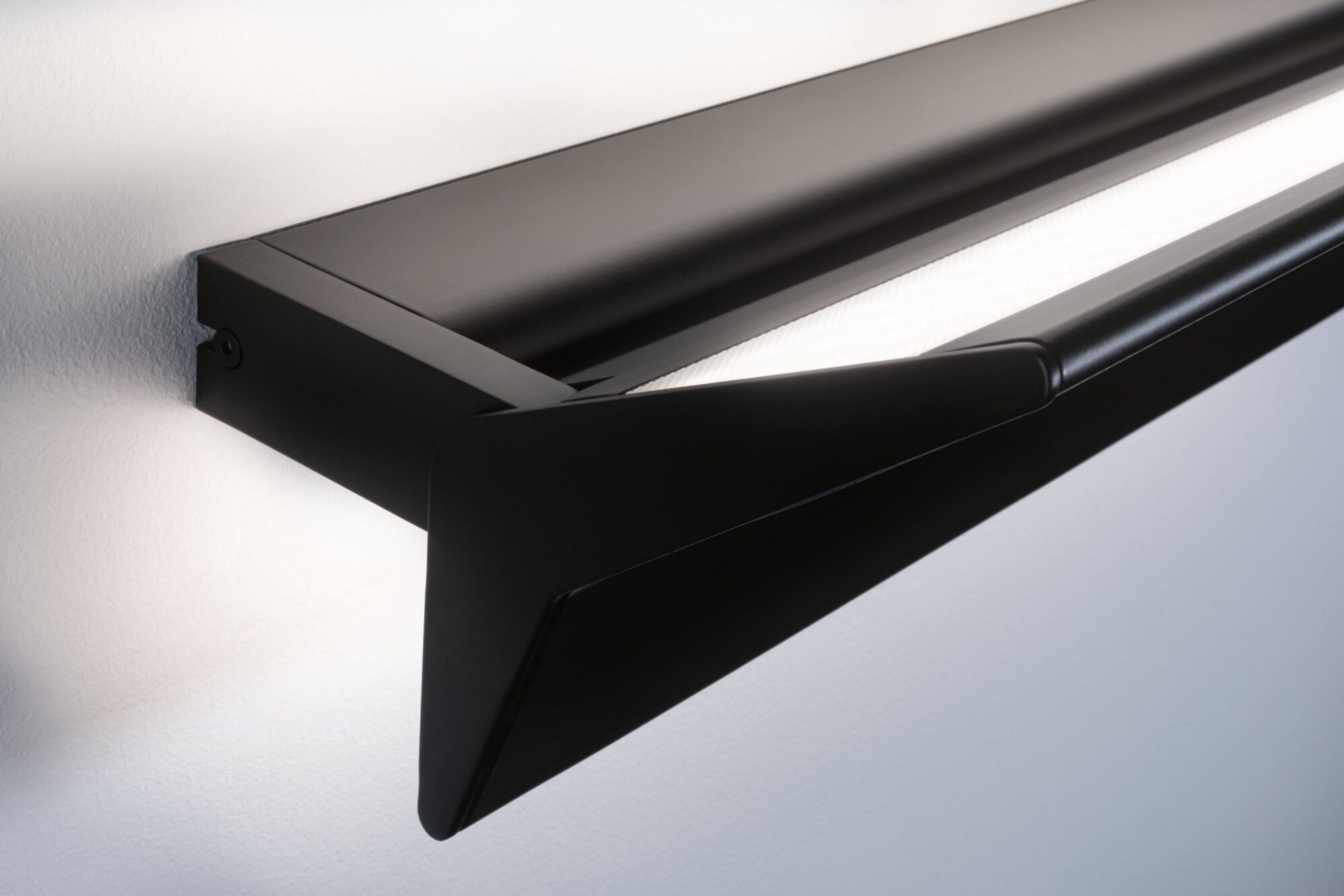 Czarny, nowoczesny kinkiet. Białe tło ściany. Światło świeci z oprawy.