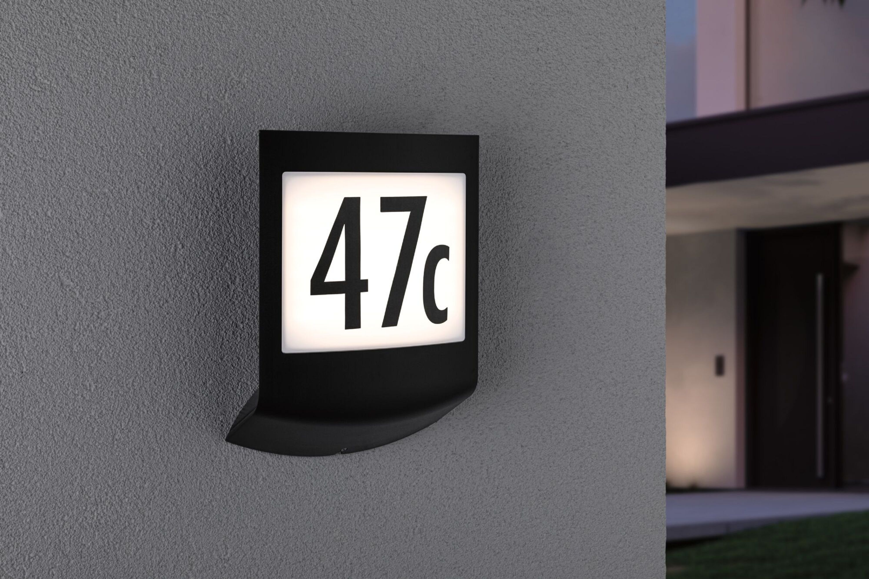 Ein schwarzes beleuchtetes Hausnummernschild. Es zeigt die Nummer „47c“ in weißer Schrift.