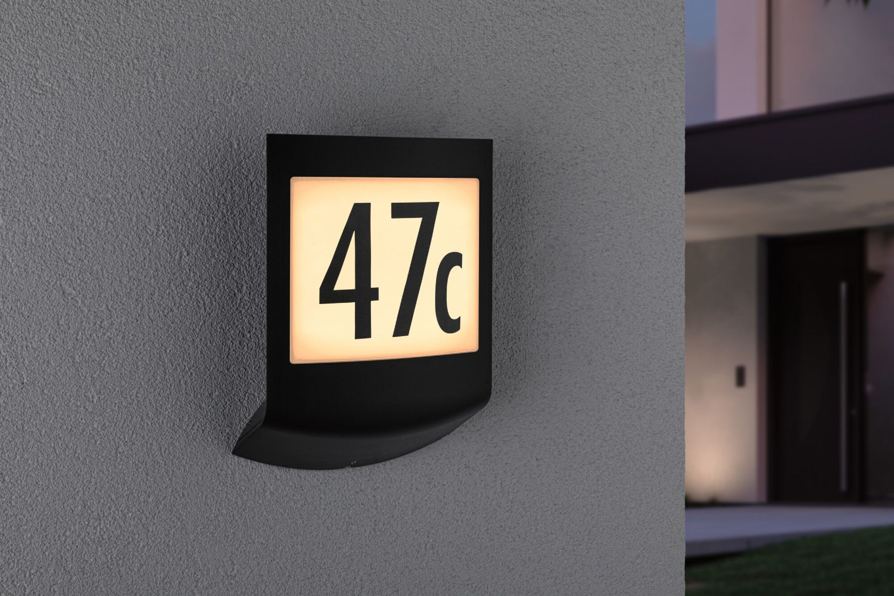 Schwarzes beleuchtetes Hausnummernschild mit der Nummer 47c an einer grauen Wand.