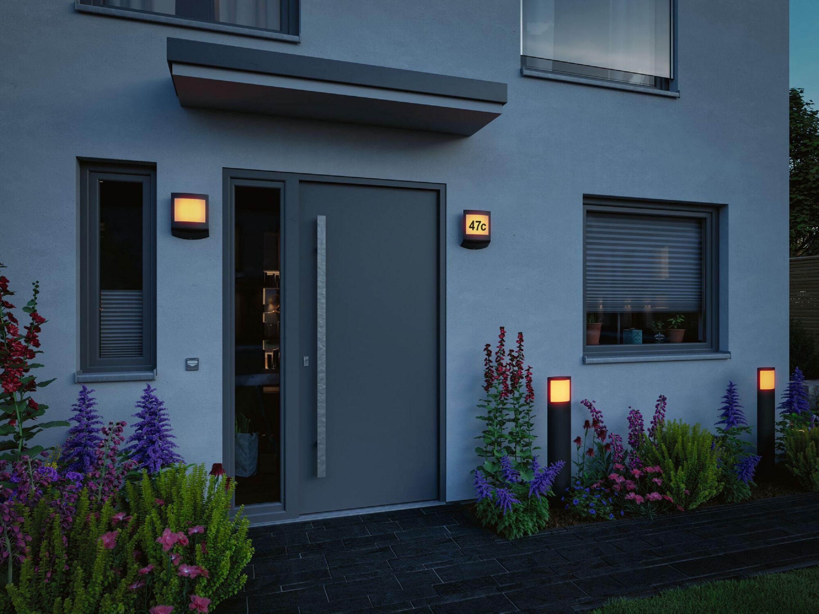 Nowoczesny dom na zewnątrz o zmierzchu z podświetlanymi drzwiami wejściowymi, światłami i krajobrazem.