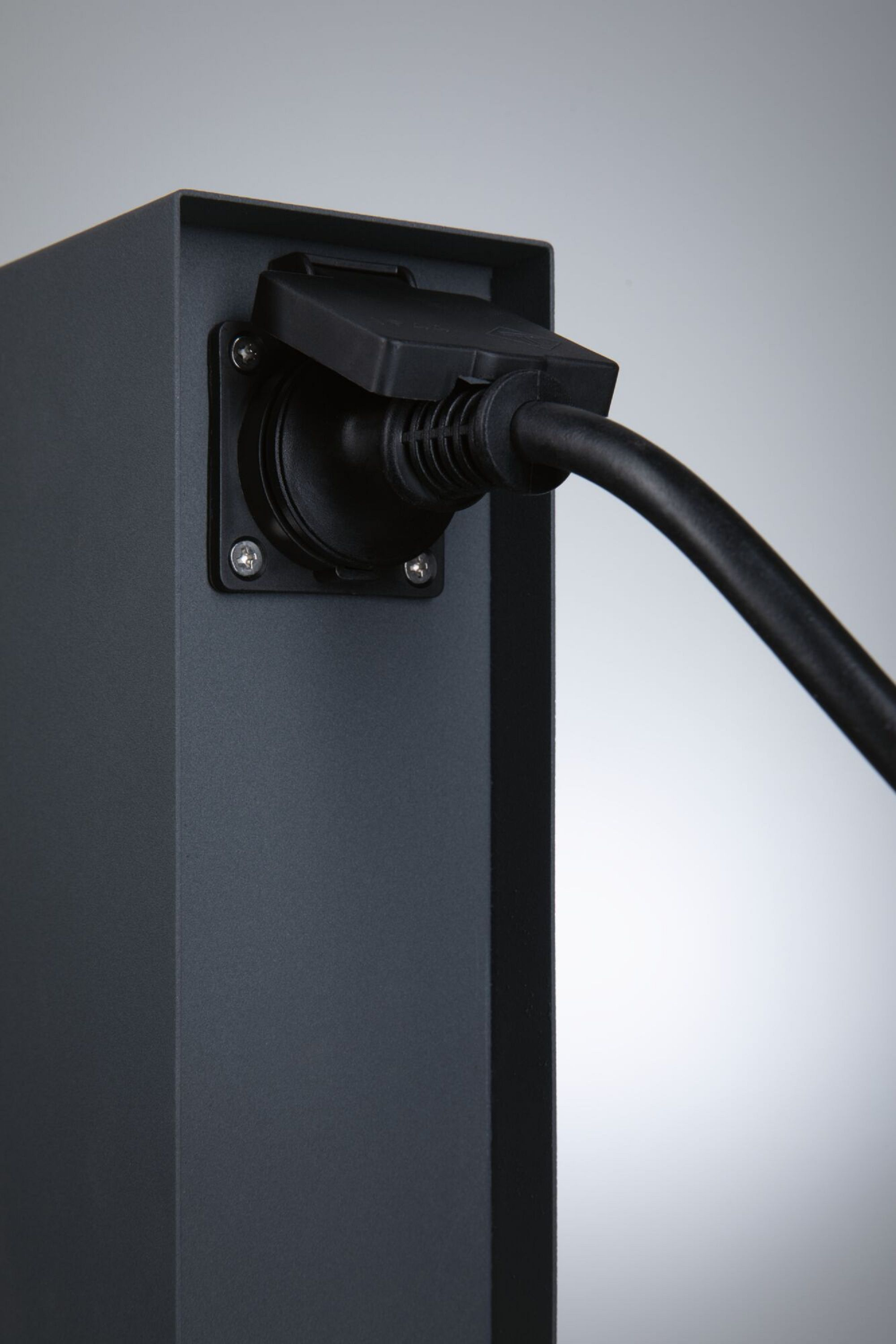 Schwarze Ladestation für Elektrofahrzeuge mit eingestecktem Kabel, auf grauem Hintergrund.