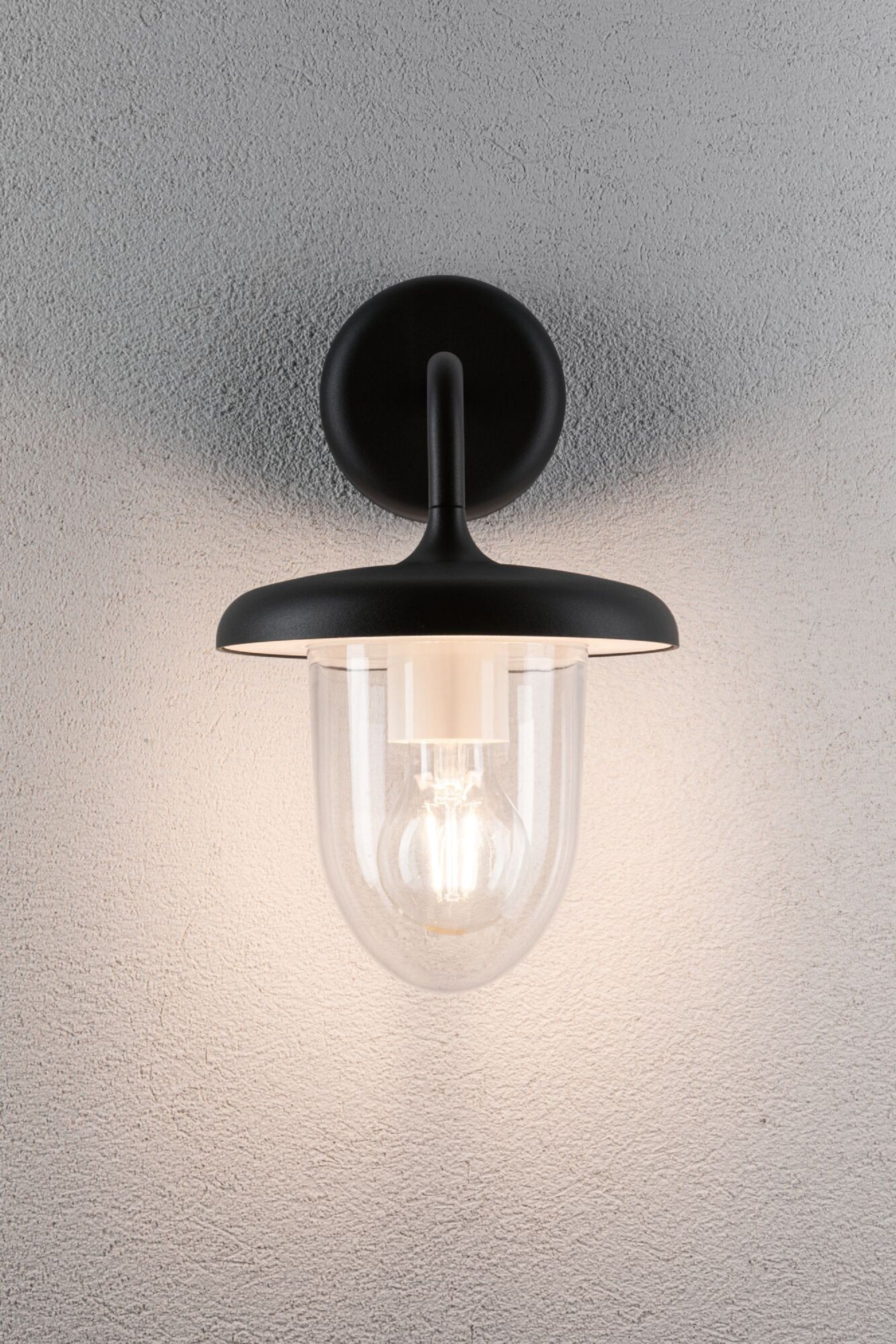 Eine schwarze Außenwandleuchte mit Glasabdeckung und sichtbarer Glühbirne, an strukturierter Wand montiert.
