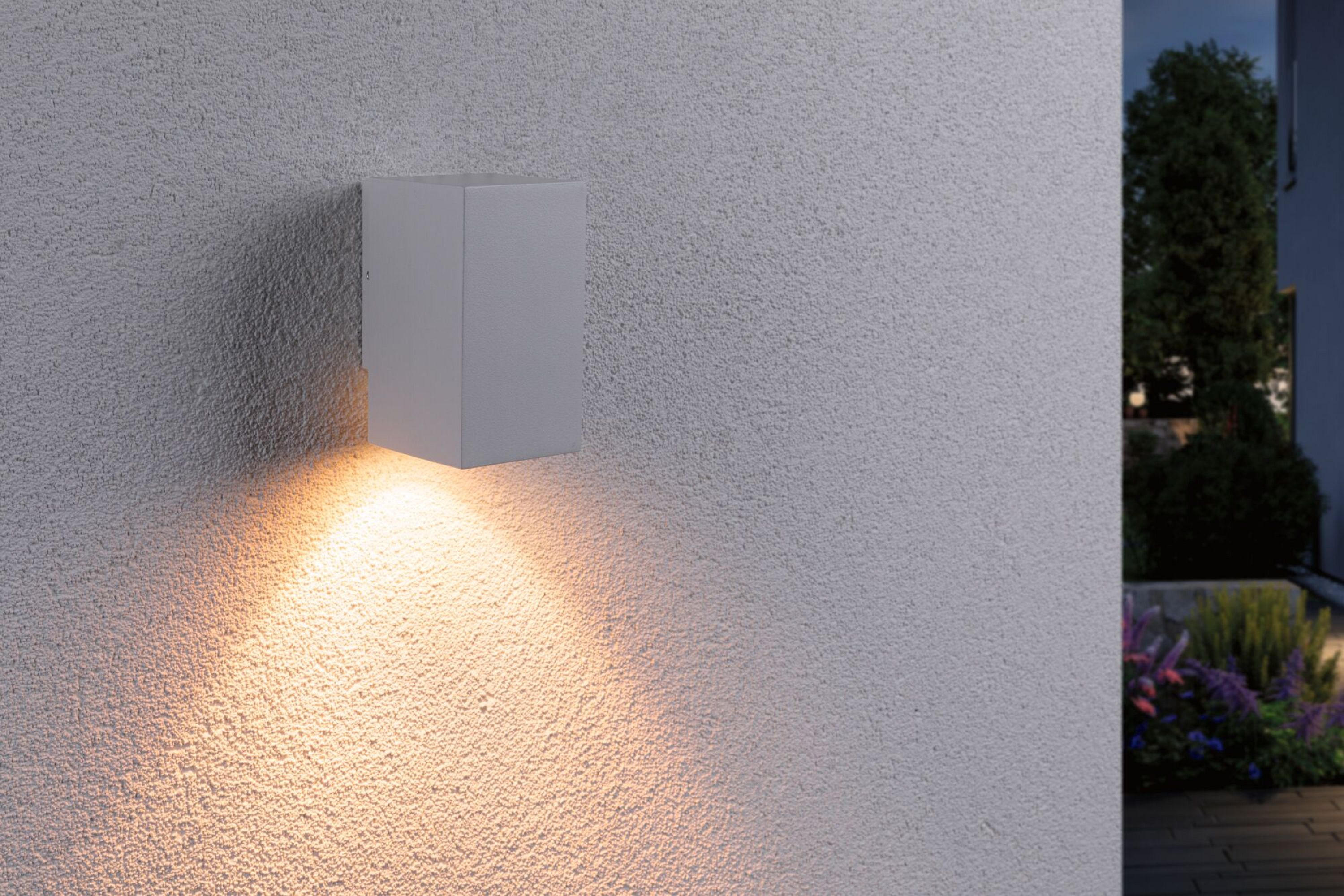 Weißer, würfelförmiger Außenwandleuchte mit warmem Licht, an strukturierter Wand.
