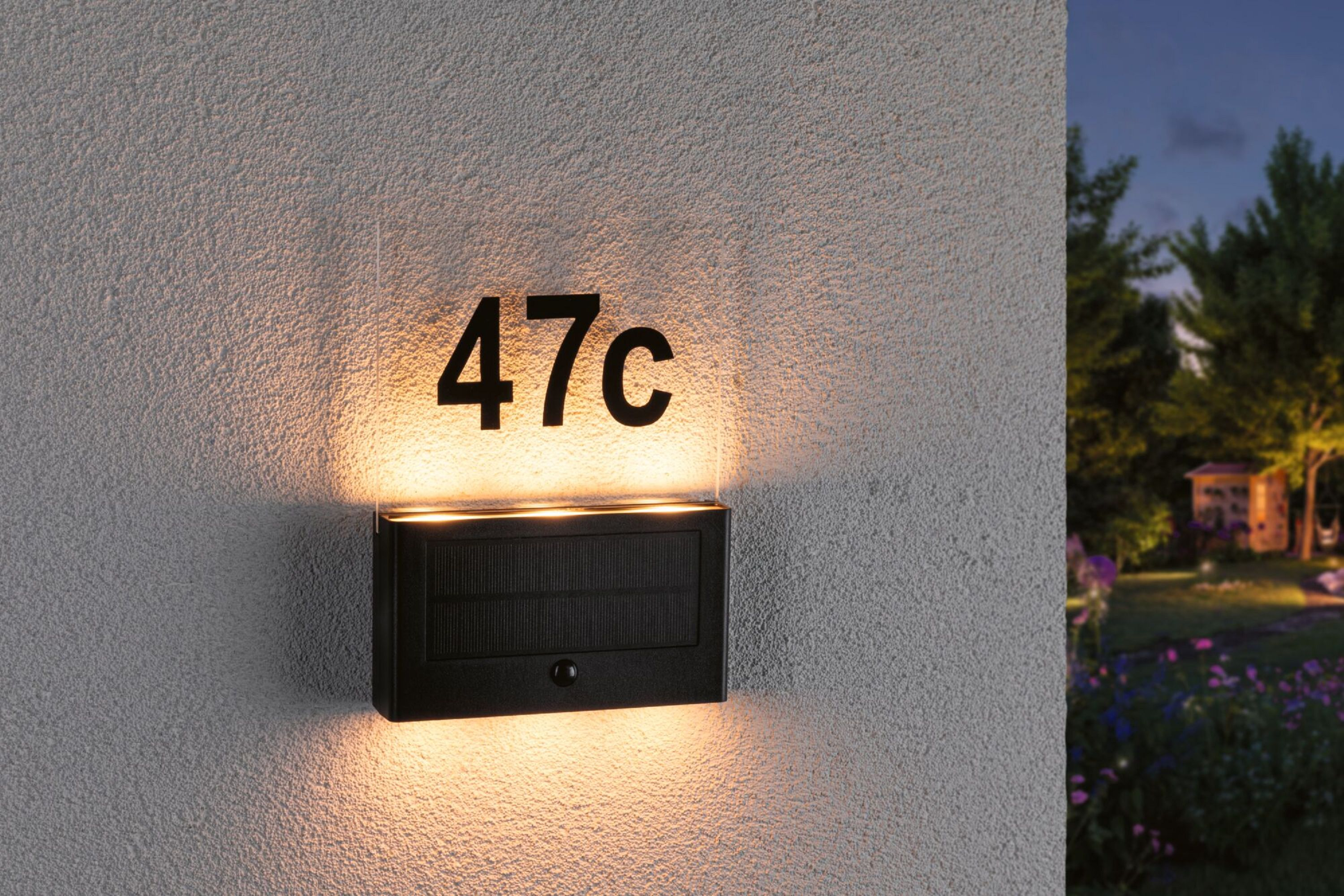 Schwarzes Hausnummernlicht mit der Nummer 47c, montiert an einer strukturierten weißen Wand.