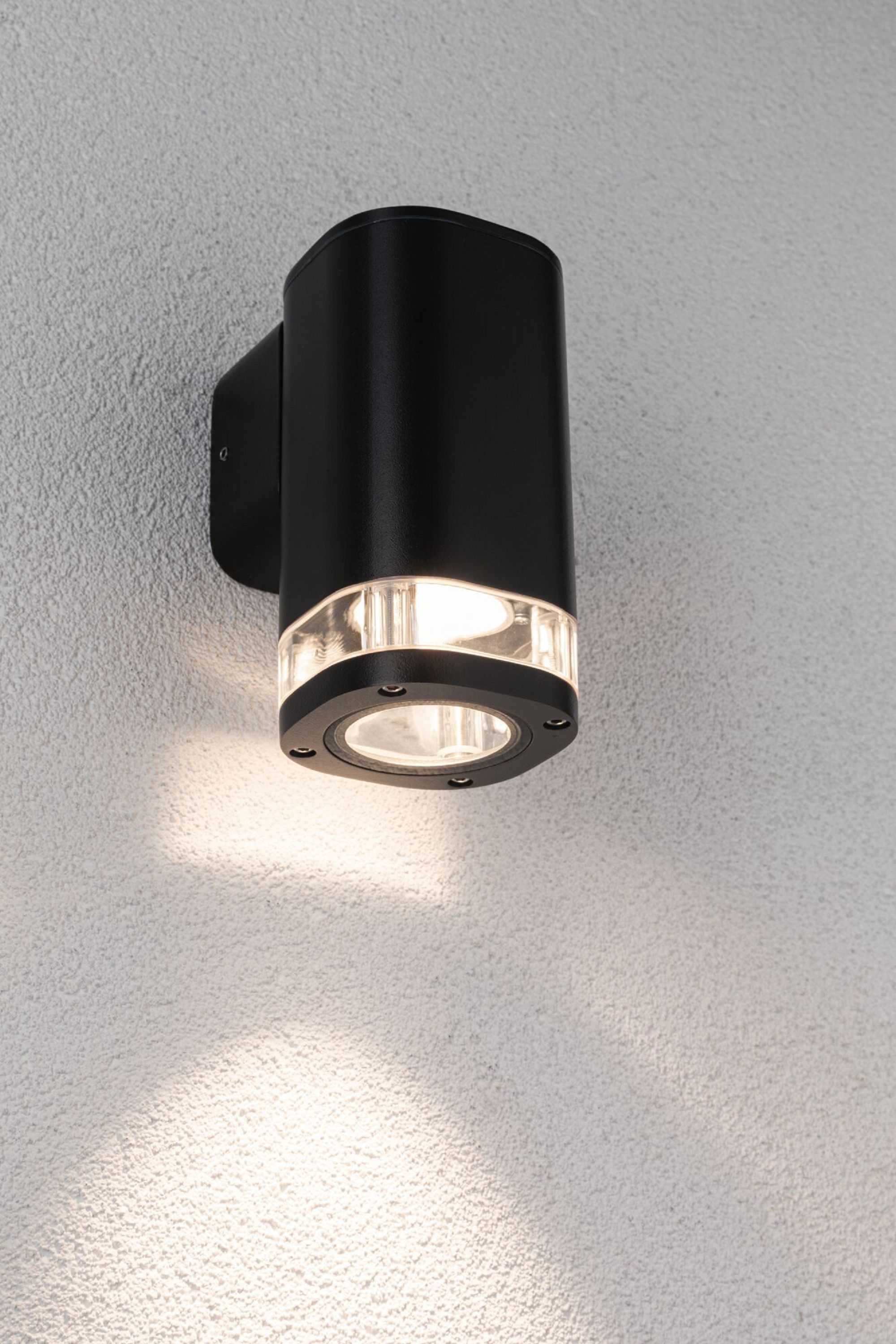 Schwarze zylindrische Außenlampe an einer weißen Wand, die nach unten leuchtet.