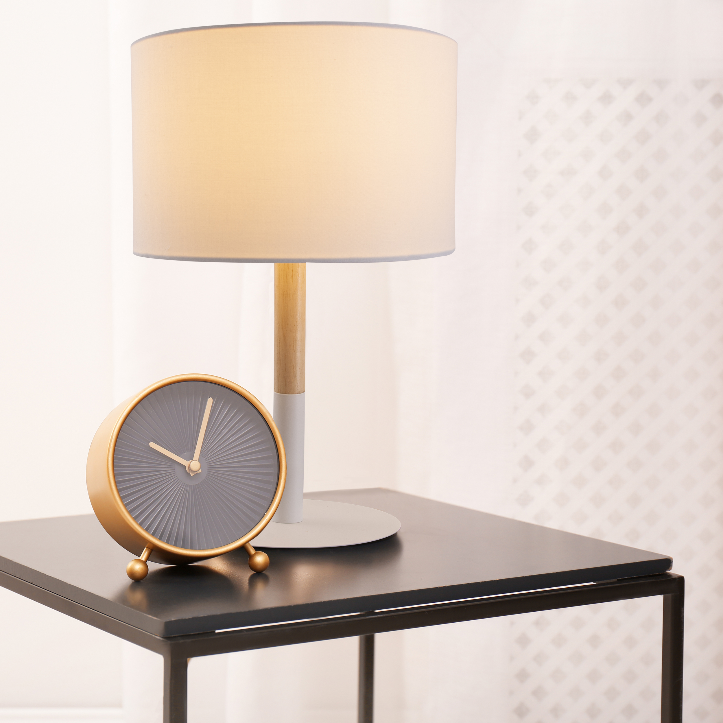 Eine Uhr und eine Lampe auf einem schwarzen Tisch. Weiße Vorhänge im Hintergrund.