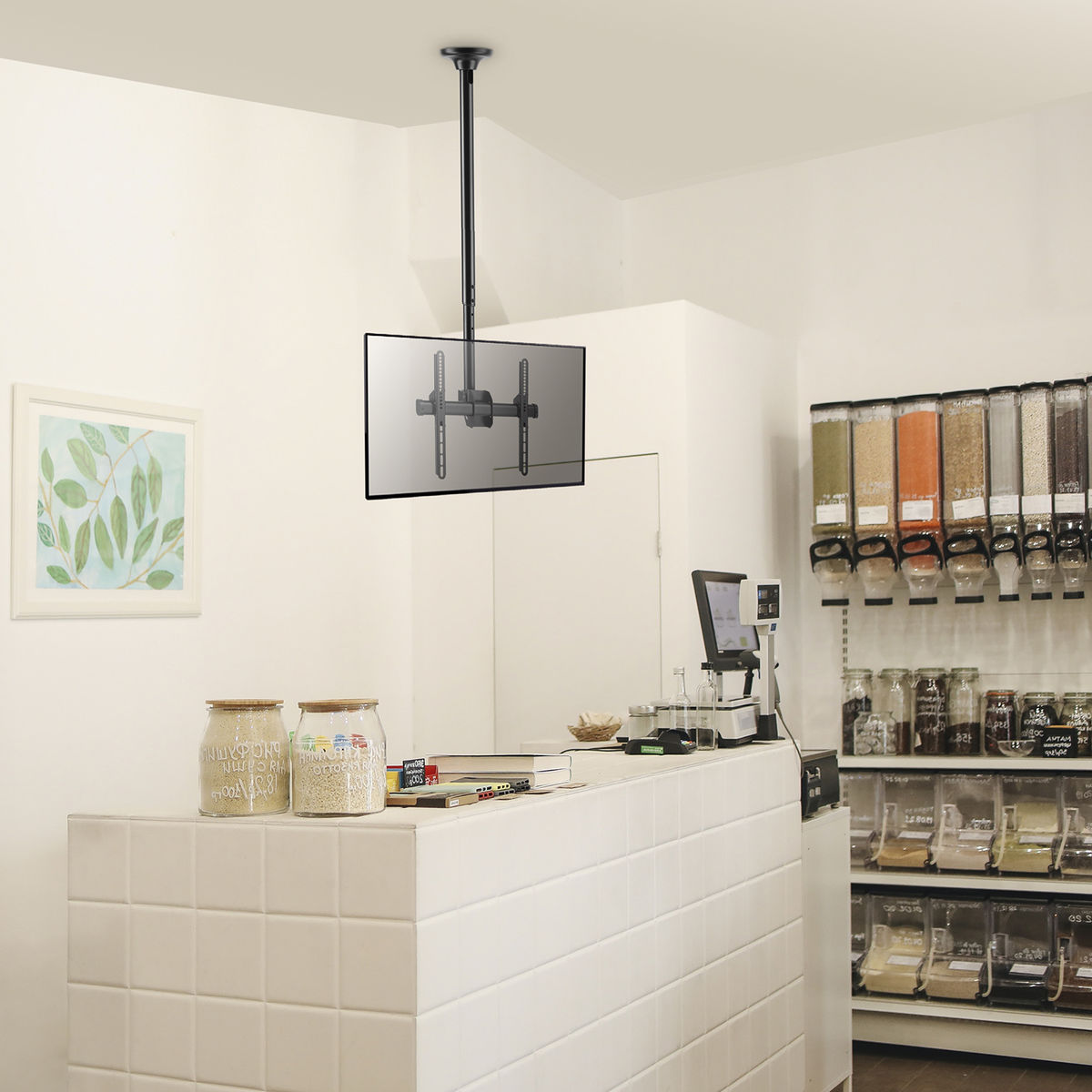 Tv aan de muur gemonteerd, in een winkel. Er zijn potten, planken en een witte toonbank.