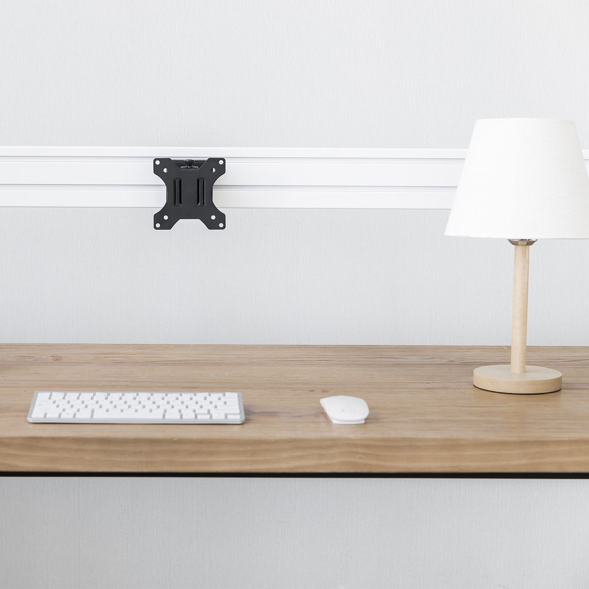Configuración de escritorio con soporte de monitor, lámpara, teclado y ratón en escritorio de madera.