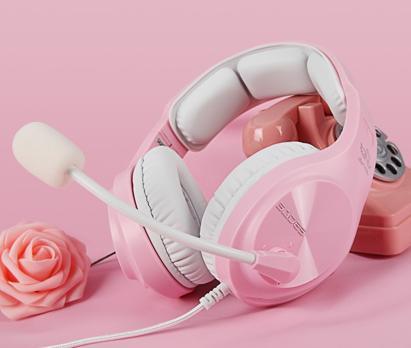 Ein rosa Headset mit Mikrofon auf rosa Hintergrund, mit rosa Rose und rosa Telefon.