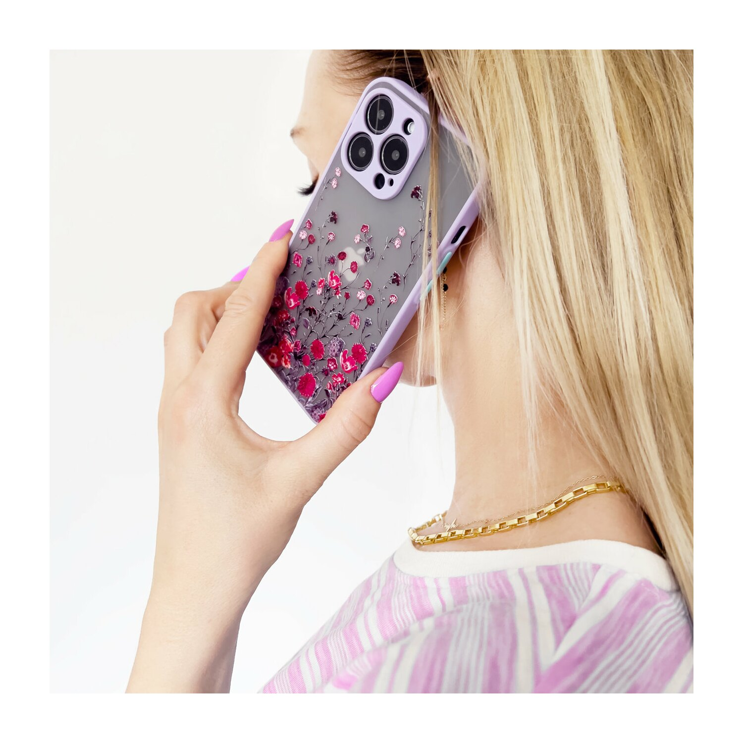 Frau hält ein Telefon mit floraler Hülle. Sie trägt eine goldene Halskette und rosa Nagellack.