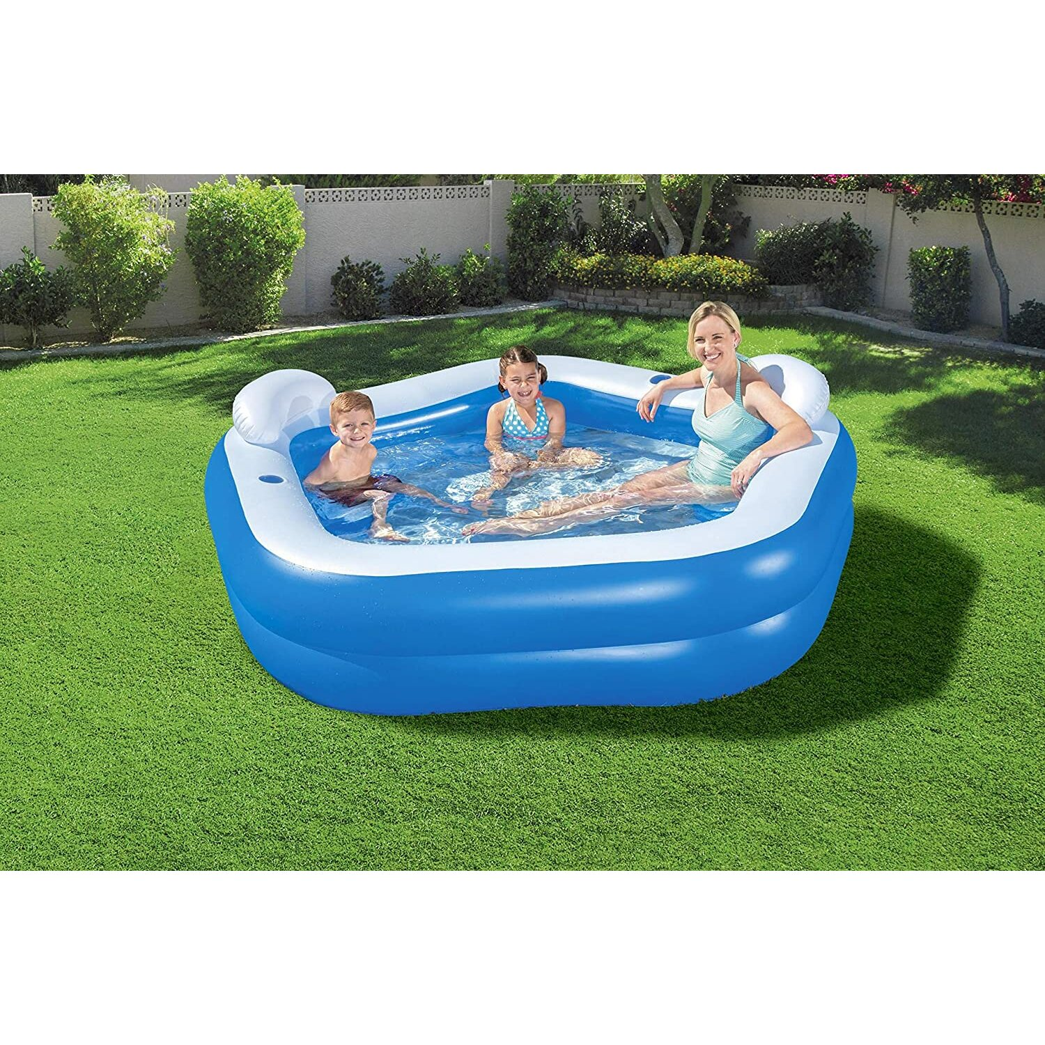 Ein blauer aufblasbarer Pool mit einer Frau und zwei Kindern darin, auf grünem Gras.