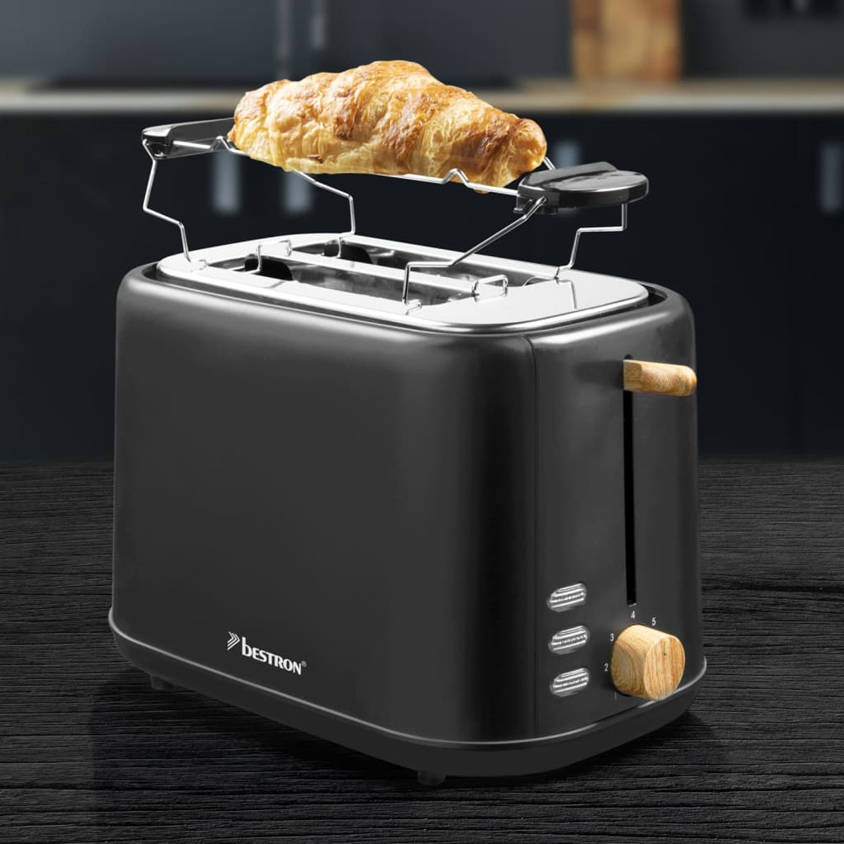 Ein schwarzer Toaster mit Holzgriff. Ein Croissant wird getoastet. Der Toaster hat ein nummeriertes Zifferblatt.