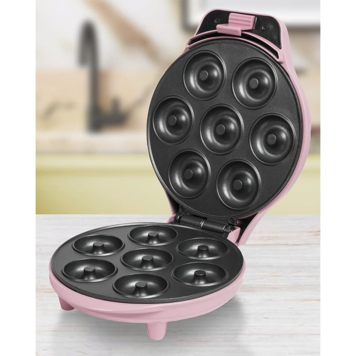 Máquina para hacer donas rosa con tapa abierta, que muestra siete moldes para donas.