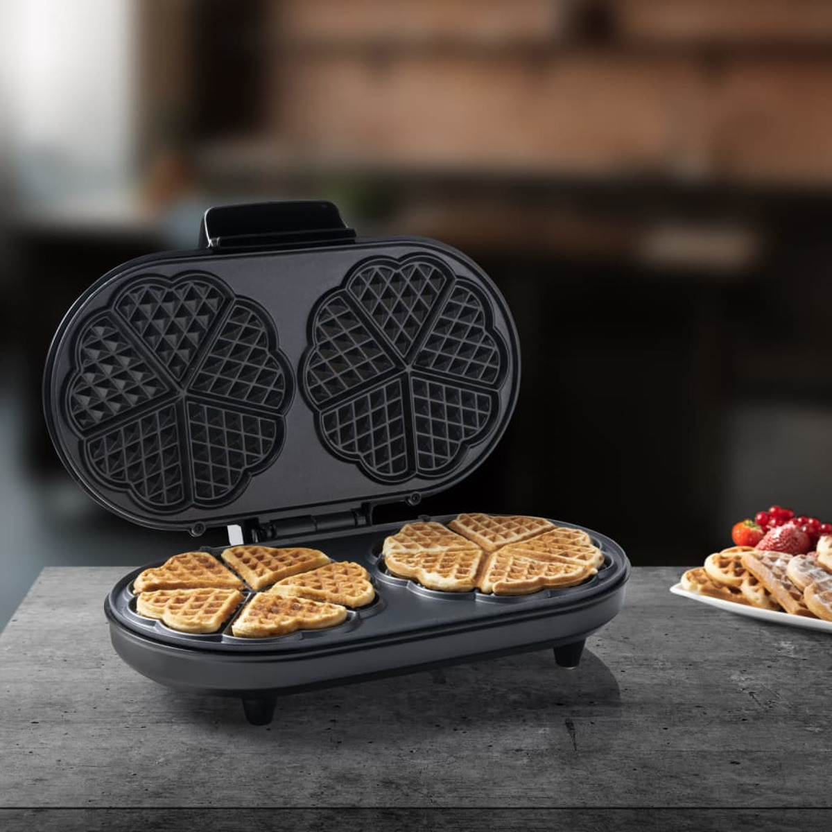 Una macchina per waffle con waffle all'interno e su un piatto. La macchina è aperta. Sfondo sfocato.