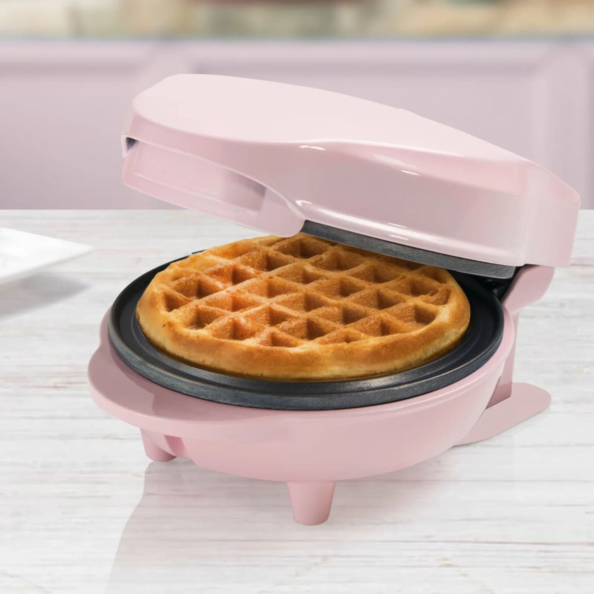 Rosa Waffeleisen mit goldbrauner Waffel darin. Das Waffeleisen ist auf einer weißen Oberfläche offen.