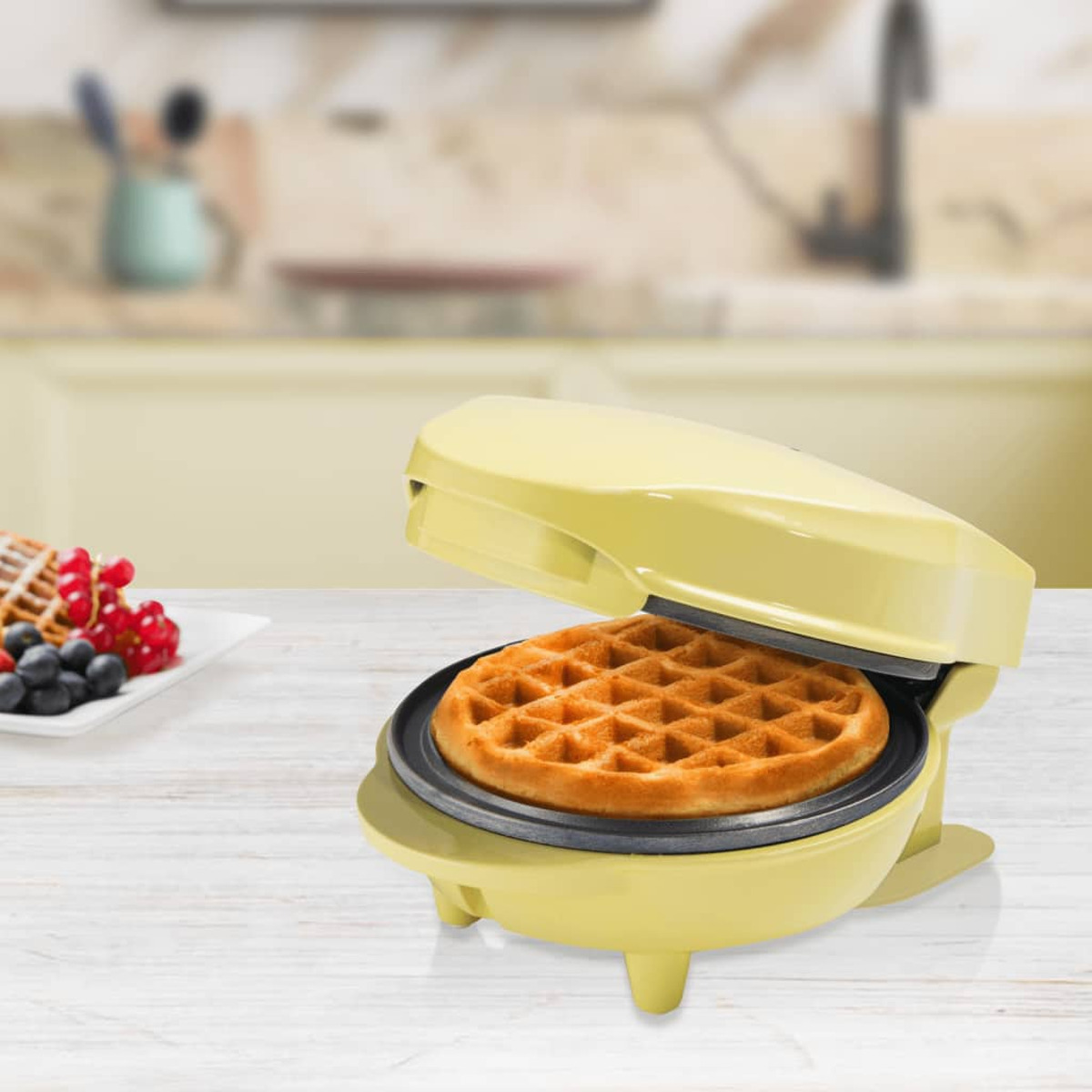 Wafflera con un gofre cocido dentro, sobre una mesa de madera. Fondo de cocina borroso.