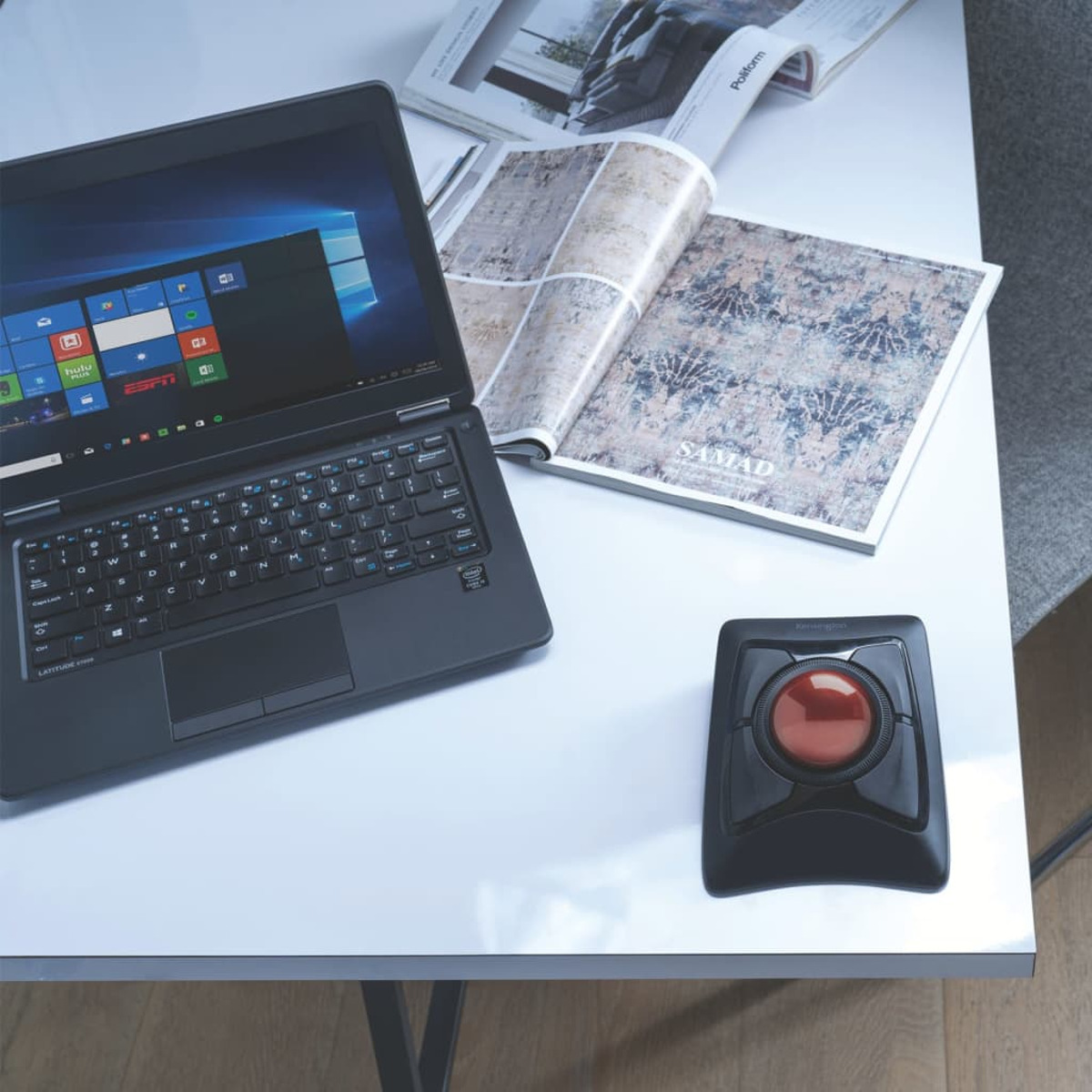Laptop, magazine, and trackball mouse on a white table. The laptop's screen is on.