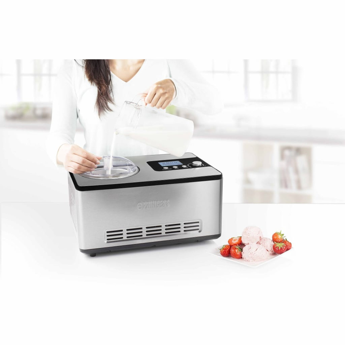 Une femme verse du liquide dans une sorbetière argentée. Des fraises sur une assiette.