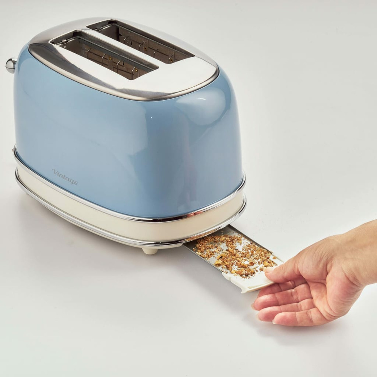 A blue and silver vintage toaster with a crumb tray being pulled out by a hand.