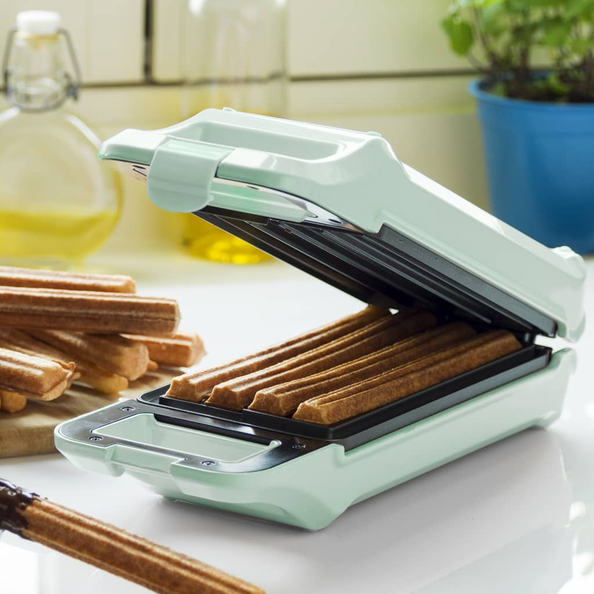 Una macchina per churros verde menta con churros all'interno e sul tavolo.