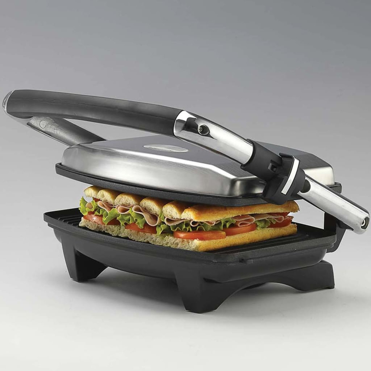 Sandwichpresse mit einem Sandwich darin. Das Sandwich enthält Tomaten, Salat und Schinken zwischen Brotscheiben.