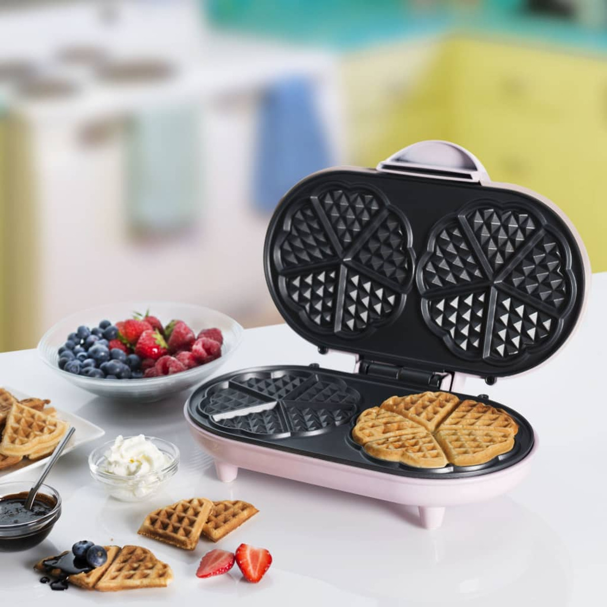 Różowa gofrownica z goframi i dodatkami na stole.