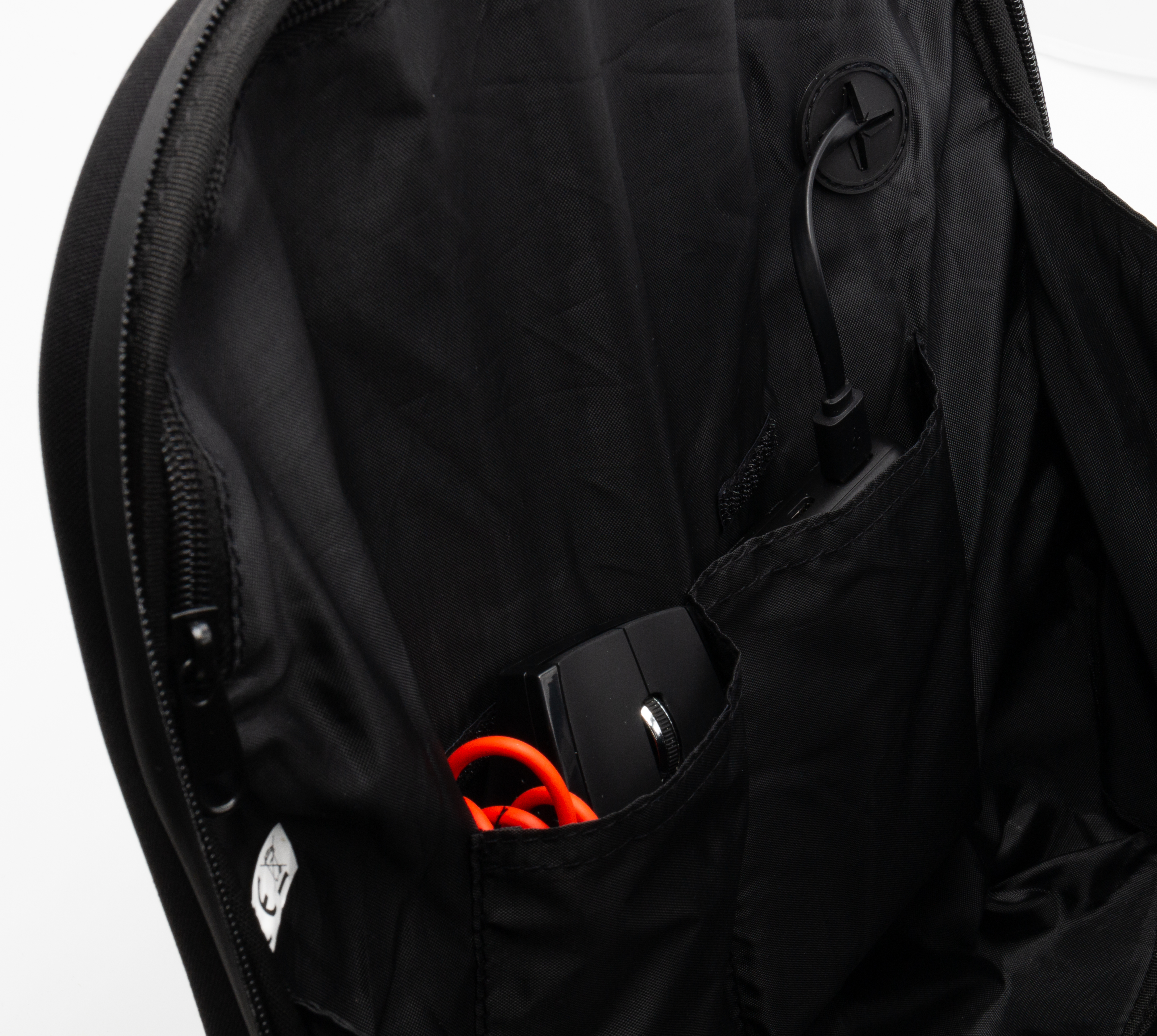 In einem schwarzen Rucksack befindet sich eine schwarze Maus mit einem orangefarbenen Ladekabel in einer Tasche.