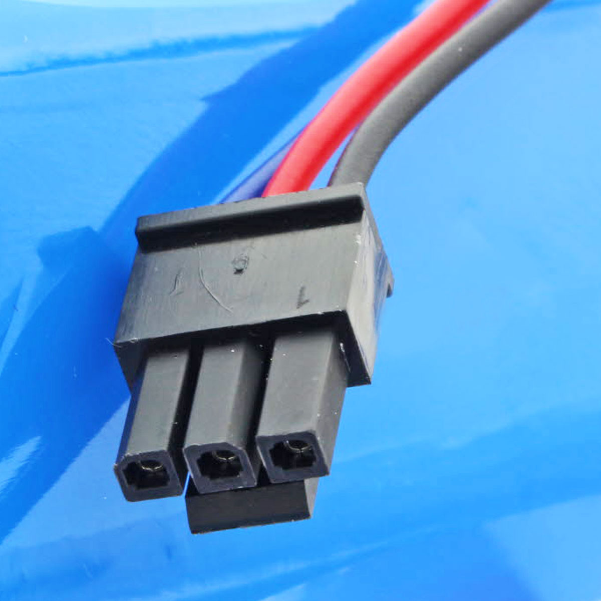 Nahaufnahme eines blauen Akkus mit einem schwarzen Stecker und drei Drähten.