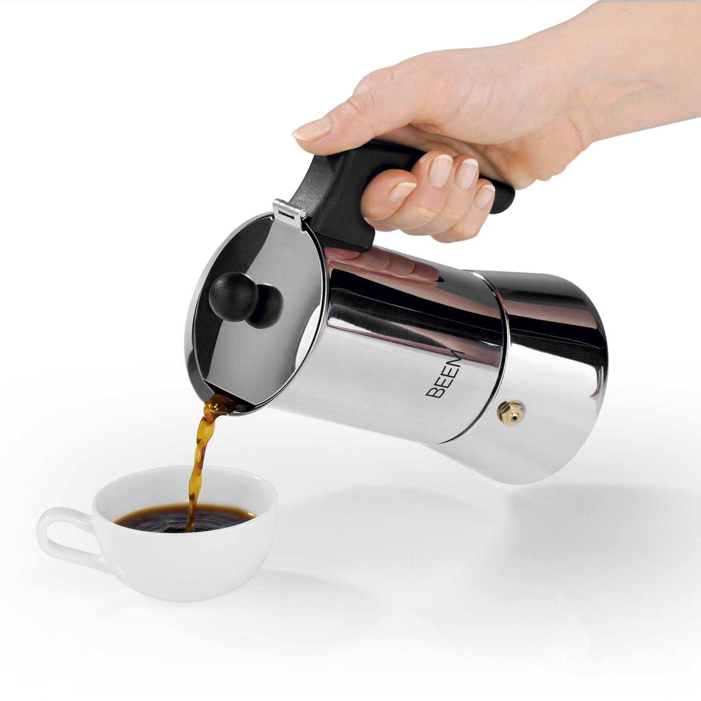 Eine Hand gießt Kaffee aus einer silbernen Mokkakanne in eine weiße Tasse auf weißer Oberfläche.