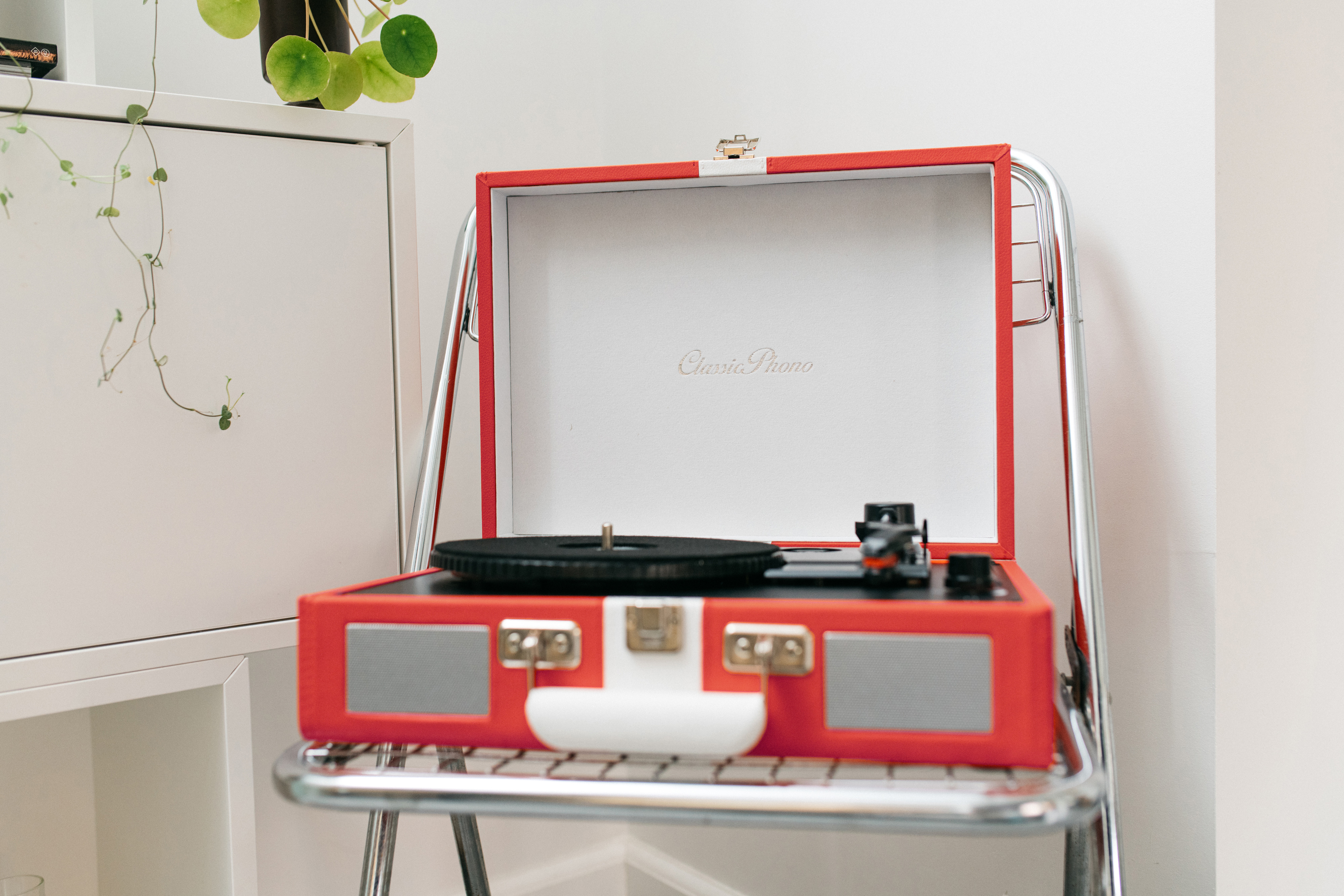 Giradischi rosso e bianco in stile vintage su un supporto argentato davanti a un mobile bianco.