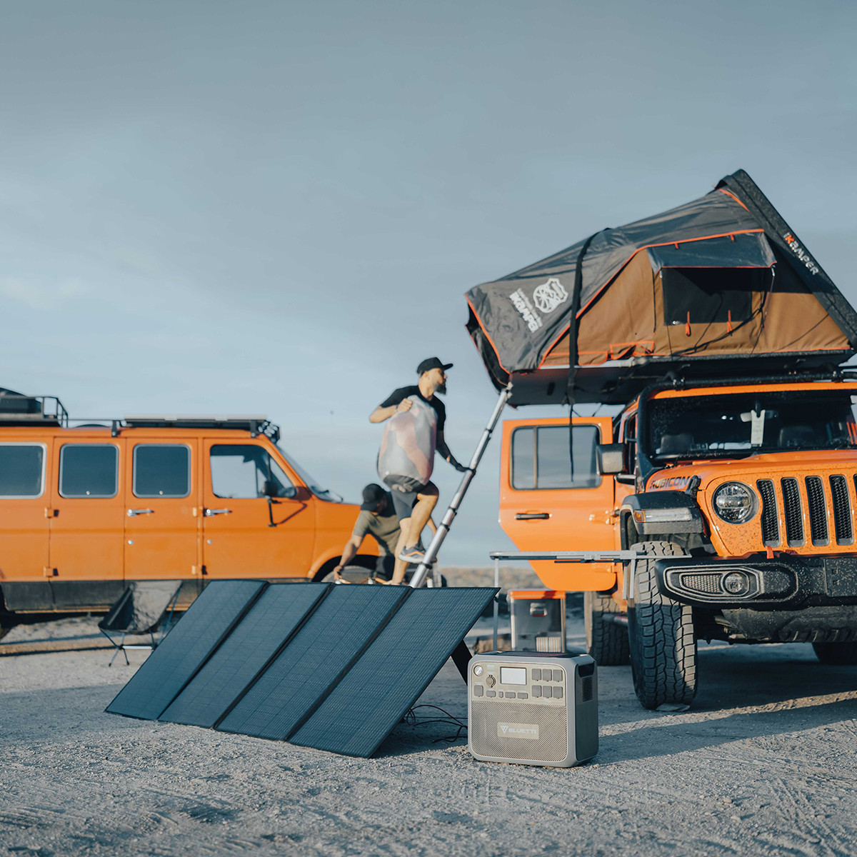 Tavan çadırlı, güneş panelli ve merdivende bir adam olan turuncu Jeep.